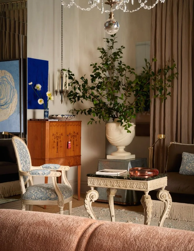 A crystal chandelier hangs above the Swedish inlaid cabinet, stone urn, and Louis XVI chair