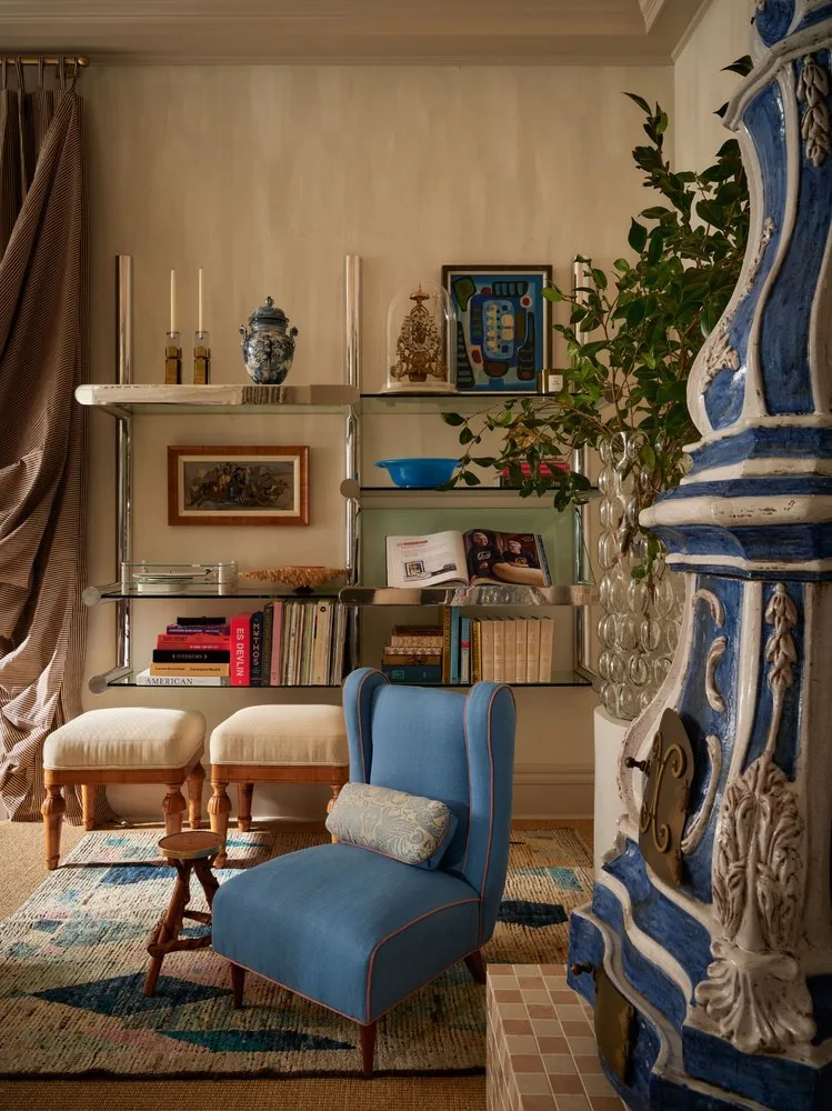 A blue Danish wing chair sits beside steel and glass shelving filled with books and Delft ceramics