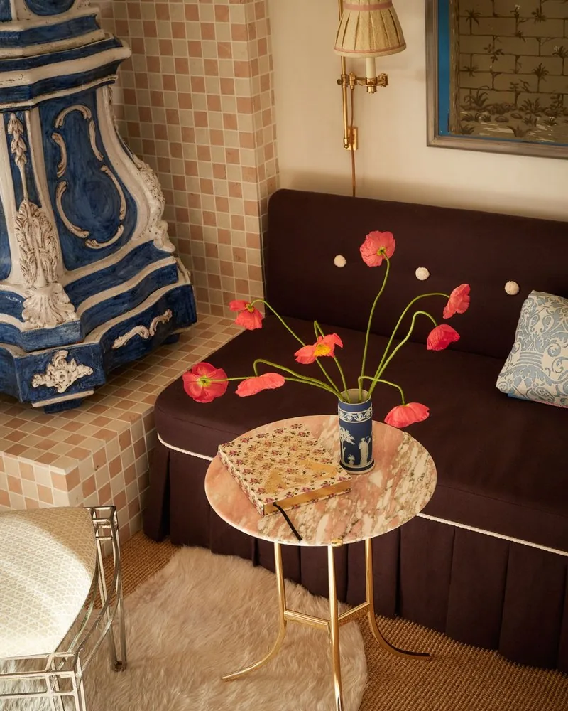 Red poppies in a Wedgwood jasperware vase top the pink marble side table beside the kachelofen