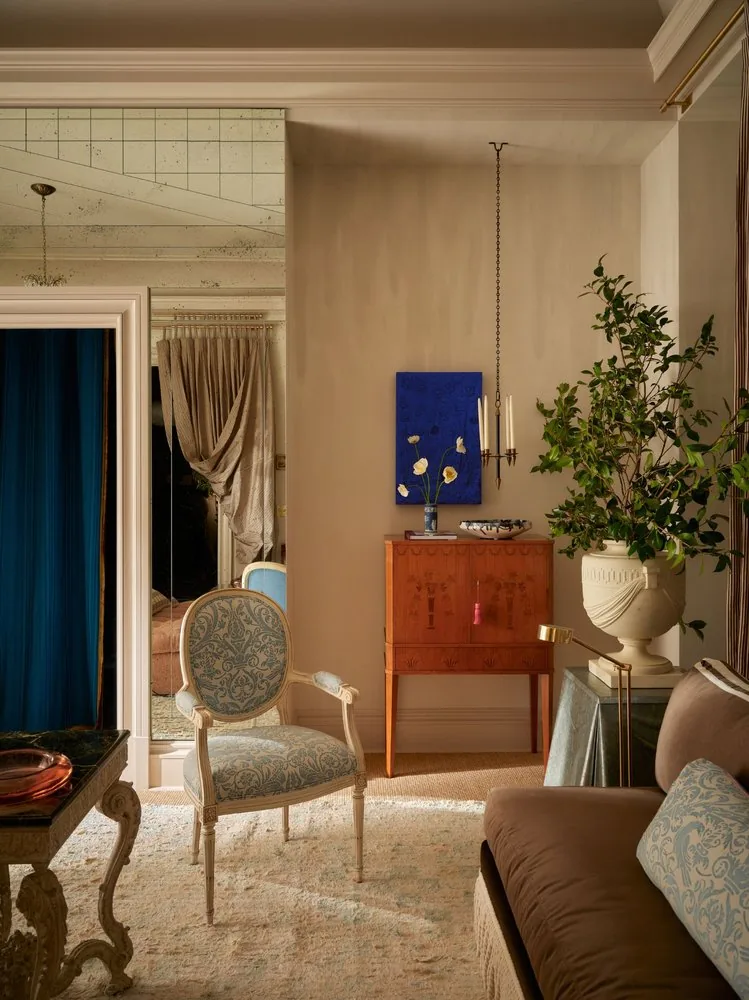 A Louis XVI fauteuil in blue damask sits beside the Swedish inlaid cabinet and a stone urn with ficus