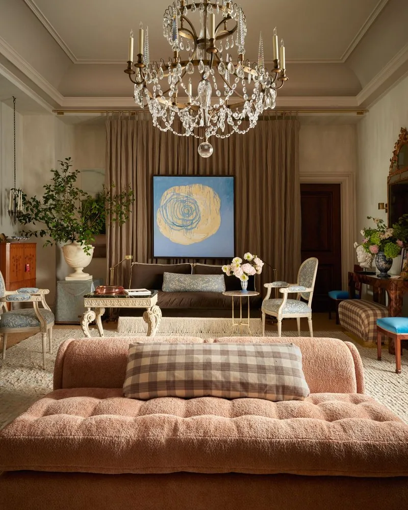 A pink bouclé sofa fronts the drawing room, with the kachelofen and chandelier beyond